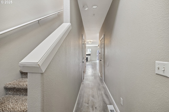 corridor featuring visible vents, wood finished floors, baseboards, and a textured wall