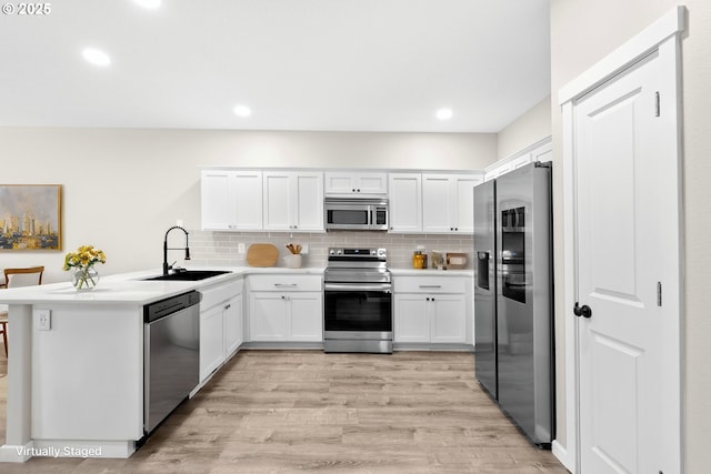 kitchen with light wood-style flooring, a peninsula, white cabinets, stainless steel appliances, and a sink