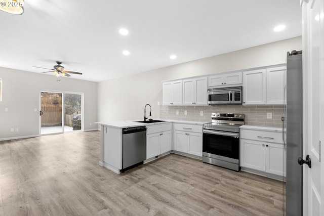 kitchen featuring light countertops, a peninsula, light wood-style floors, stainless steel appliances, and a sink