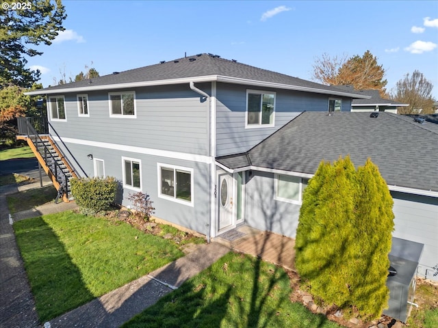 back of property with a yard, stairway, and roof with shingles