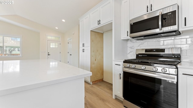 kitchen featuring lofted ceiling, appliances with stainless steel finishes, light hardwood / wood-style floors, white cabinets, and decorative backsplash