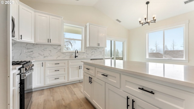 kitchen with sink, stainless steel gas stove, white cabinetry, vaulted ceiling, and light wood-type flooring