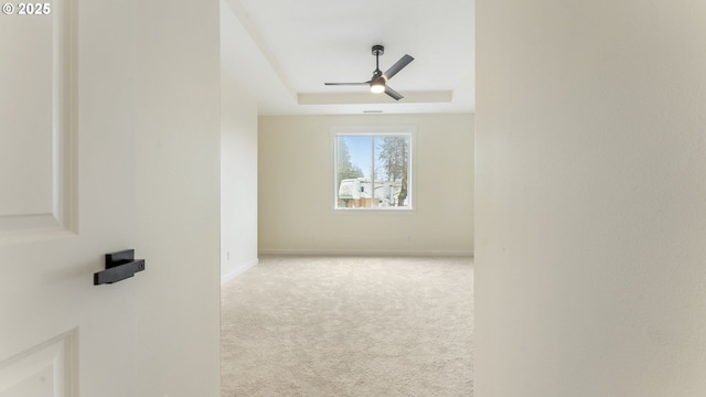 spare room featuring a raised ceiling, light colored carpet, and ceiling fan