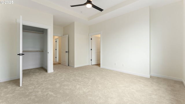 unfurnished bedroom featuring a closet, light colored carpet, a raised ceiling, and ceiling fan