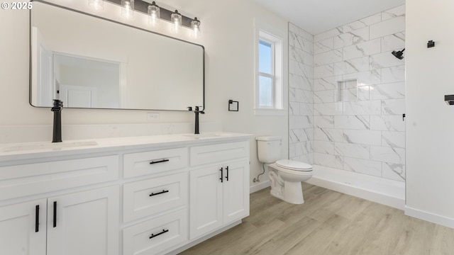 bathroom featuring hardwood / wood-style flooring, tiled shower, vanity, and toilet