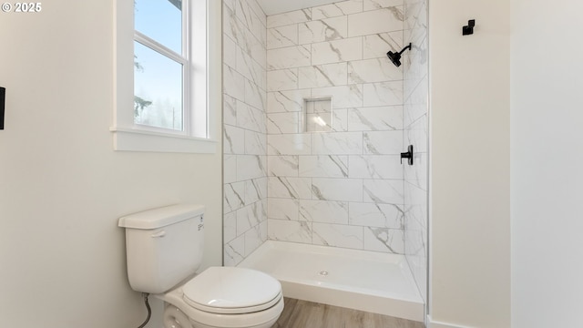 bathroom featuring hardwood / wood-style flooring, a tile shower, and toilet