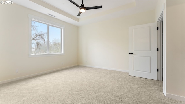 spare room featuring ceiling fan, light colored carpet, and a tray ceiling