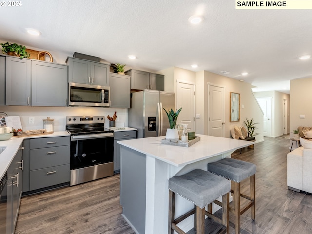 kitchen featuring a breakfast bar area, appliances with stainless steel finishes, gray cabinetry, dark hardwood / wood-style flooring, and a center island