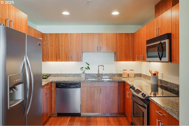 kitchen with stainless steel appliances, stone countertops, sink, and light wood-type flooring