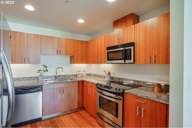 kitchen featuring sink, light hardwood / wood-style flooring, stainless steel appliances, and stone counters