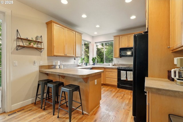 8503 SE 139th Ct, Portland, OR 97236 - kitchen featuring black appliances, light brown cabinets, a peninsula, a breakfast bar, and light wood-type flooring