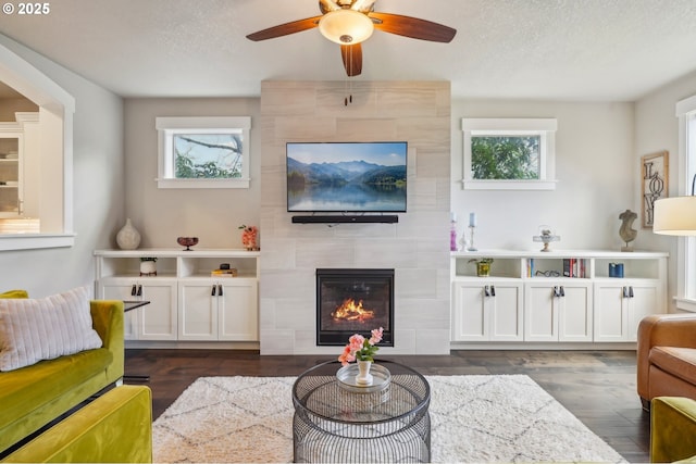 living area with a textured ceiling, a healthy amount of sunlight, dark wood-style floors, and a fireplace