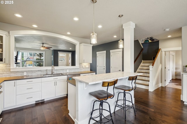 kitchen featuring ceiling fan, dark wood finished floors, arched walkways, white cabinetry, and a sink