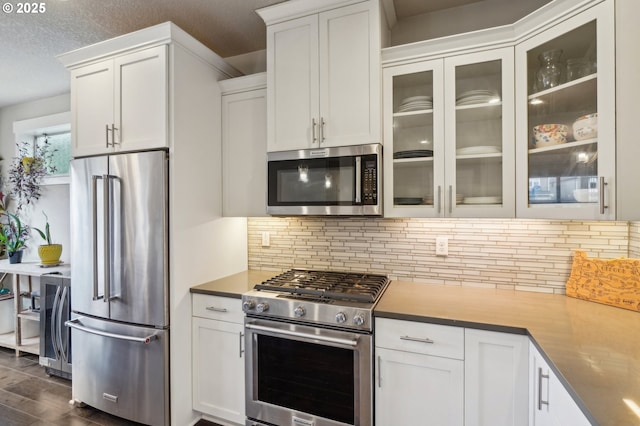 kitchen featuring white cabinets, high end appliances, glass insert cabinets, and tasteful backsplash