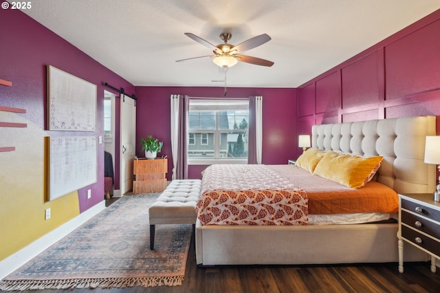 bedroom featuring a barn door, baseboards, wood finished floors, and a ceiling fan