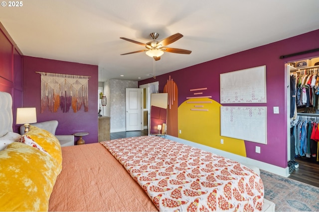 bedroom featuring a walk in closet, ceiling fan, baseboards, wood finished floors, and a closet