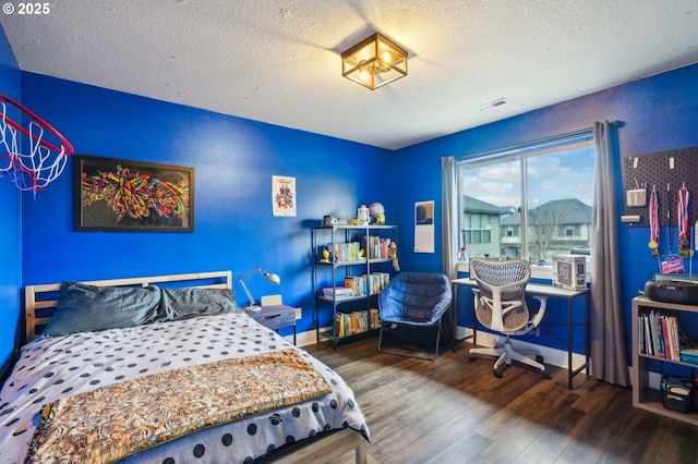 bedroom with visible vents, a textured ceiling, baseboards, and wood finished floors