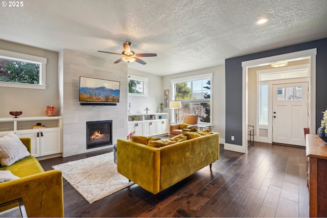 living area with dark wood finished floors, a tile fireplace, a textured ceiling, and baseboards