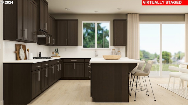 kitchen featuring a breakfast bar, under cabinet range hood, a kitchen island, light countertops, and stainless steel gas cooktop