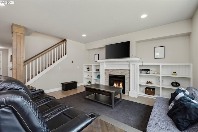 living room featuring a stone fireplace, recessed lighting, wood finished floors, and stairway