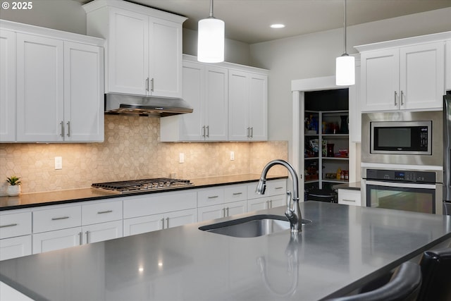 kitchen featuring white cabinets, dark countertops, appliances with stainless steel finishes, a sink, and under cabinet range hood