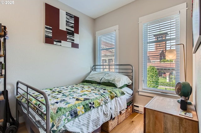 bedroom featuring baseboard heating, multiple windows, and wood finished floors
