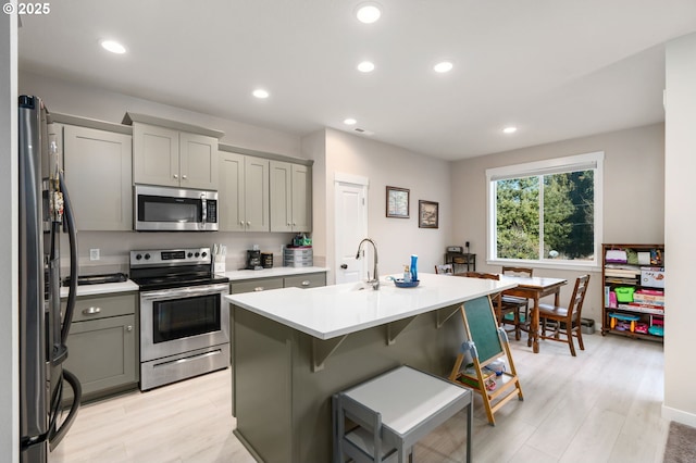 kitchen with light wood finished floors, stainless steel appliances, light countertops, and gray cabinetry