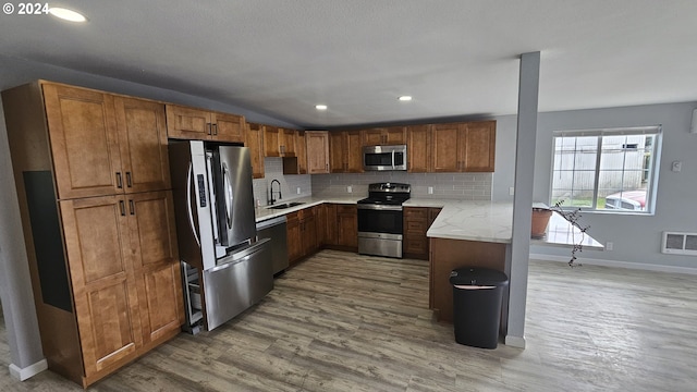 kitchen with light hardwood / wood-style floors, appliances with stainless steel finishes, tasteful backsplash, light stone countertops, and sink