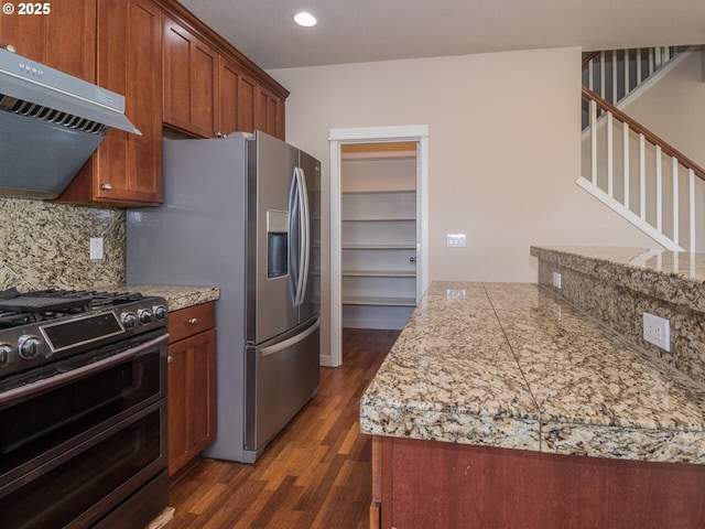 kitchen with decorative backsplash, appliances with stainless steel finishes, dark wood finished floors, range hood, and brown cabinetry