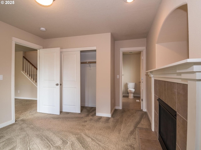unfurnished bedroom featuring carpet, a tiled fireplace, baseboards, and a closet
