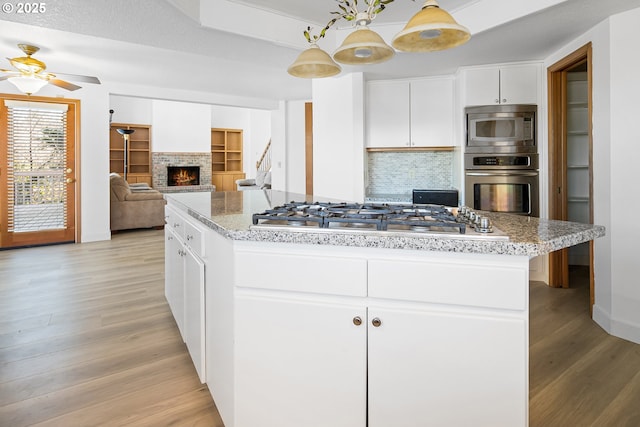 kitchen featuring white cabinetry, hanging light fixtures, stainless steel appliances, light hardwood / wood-style floors, and a kitchen island