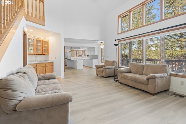 living room featuring a towering ceiling, wet bar, ceiling fan, and light hardwood / wood-style flooring