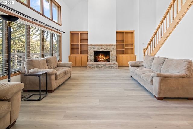 living room with a high ceiling, a healthy amount of sunlight, a fireplace, and light hardwood / wood-style floors