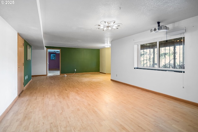 empty room with a notable chandelier, light hardwood / wood-style floors, and a textured ceiling