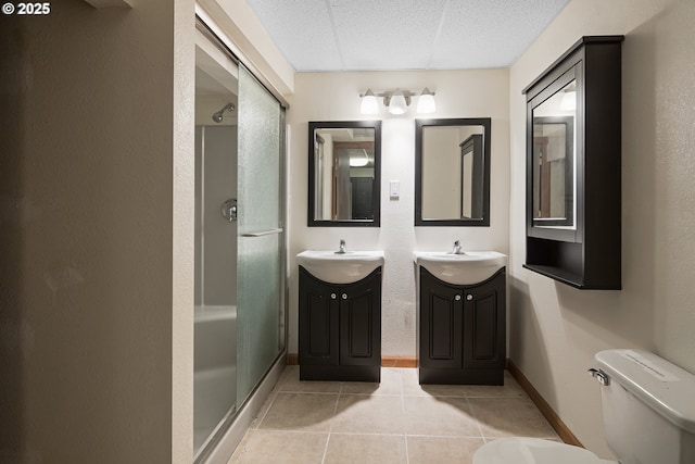 bathroom with a paneled ceiling, vanity, a shower with shower door, tile patterned floors, and toilet