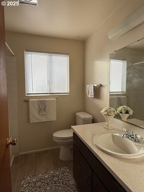 full bathroom featuring toilet, wood finished floors, vanity, baseboards, and a shower