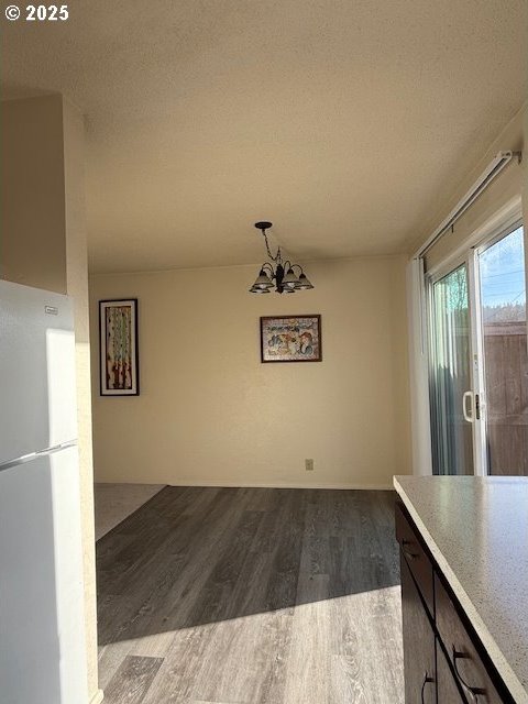 unfurnished dining area with a chandelier, dark wood-style flooring, and a textured ceiling