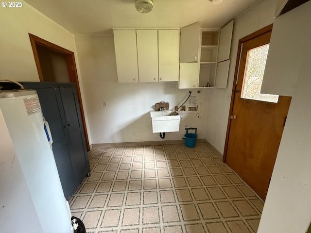 washroom featuring cabinet space, light floors, baseboards, and a sink