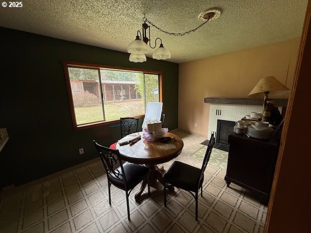 dining space with tile patterned floors, a notable chandelier, a fireplace, and a textured ceiling