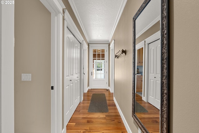 hallway with a textured ceiling, light hardwood / wood-style floors, and ornamental molding