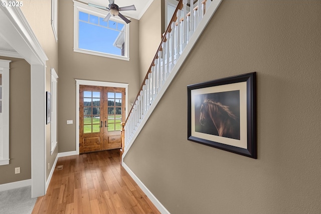 foyer entrance with ceiling fan, french doors, light hardwood / wood-style flooring, crown molding, and a towering ceiling