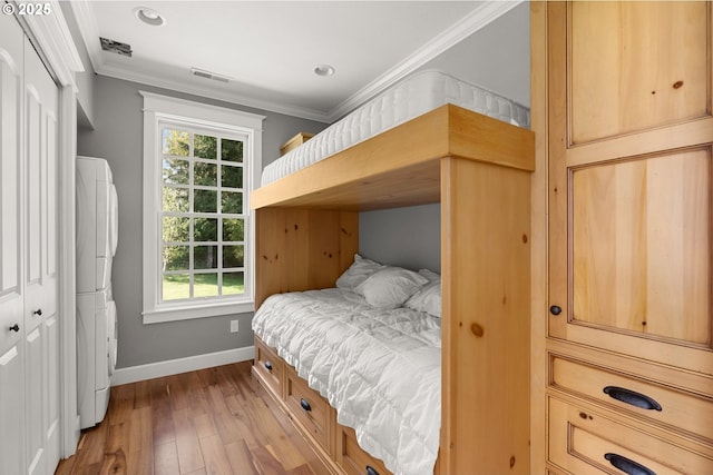 bedroom with multiple windows, stacked washing maching and dryer, ornamental molding, and a closet