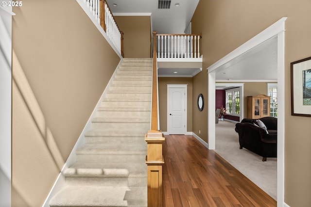 stairway with crown molding and wood-type flooring