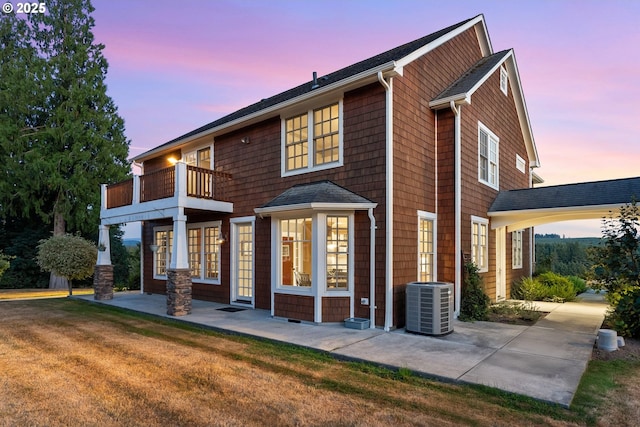 back house at dusk featuring a balcony, a lawn, and central air condition unit