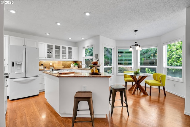 12909 SW Jacob Ct, Portland, OR 97224 - kitchen with white refrigerator with ice dispenser, a textured ceiling, a kitchen island, healthy amount of natural light, and glass insert cabinets
