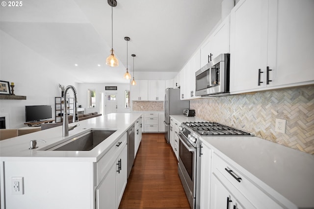 kitchen with appliances with stainless steel finishes, a sink, a kitchen island with sink, open floor plan, and decorative backsplash