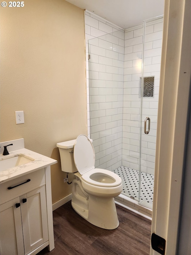 bathroom with vanity, toilet, baseboards, wood finished floors, and a stall shower