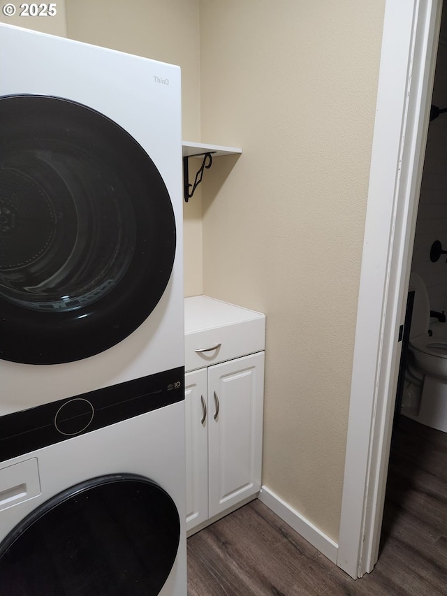 clothes washing area with dark wood-type flooring, stacked washer and dryer, and baseboards