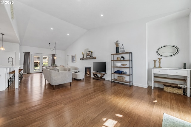 living room featuring recessed lighting, high vaulted ceiling, wood finished floors, and a lit fireplace