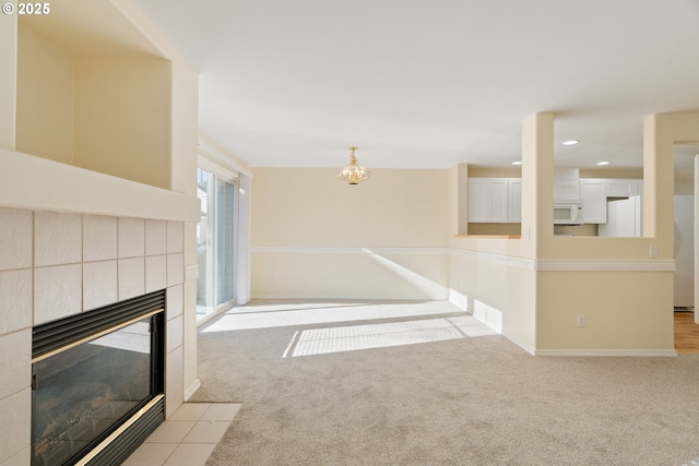 unfurnished living room featuring a tile fireplace, light carpet, and a chandelier